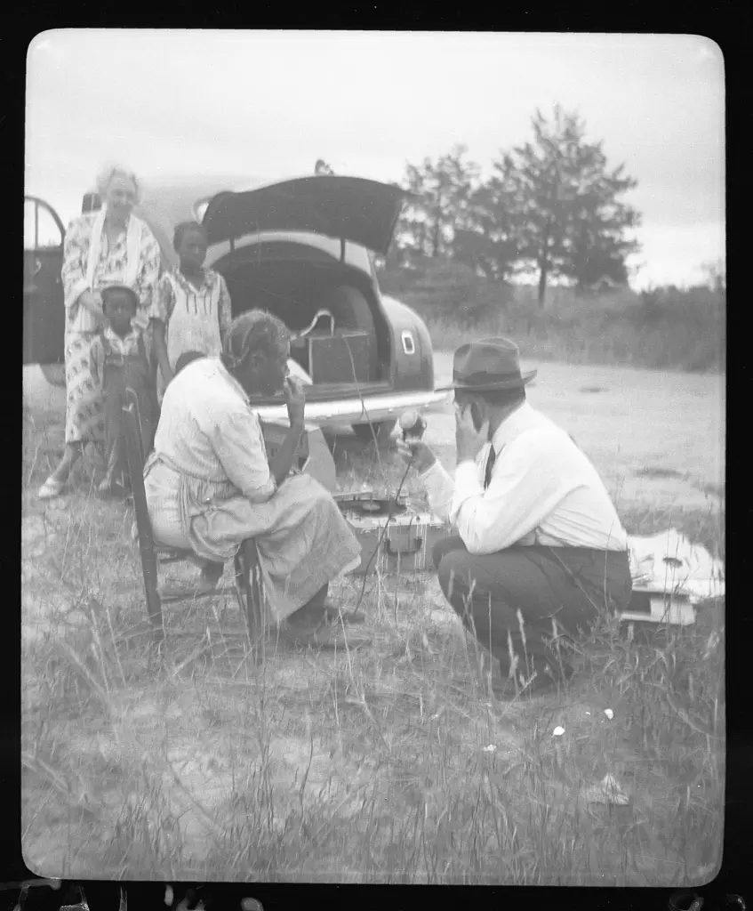 Aunt Harriett McClintock at the microphone with John A. Lomax, Sr., Mrs. Ruby Pickens Tartt, and Aunt Harriett's 'great-grands' children in background, at crossroads near Sumterville, Alabama